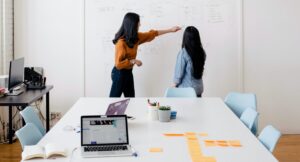 Businesswomen review experience data and flowcharts on whiteboard